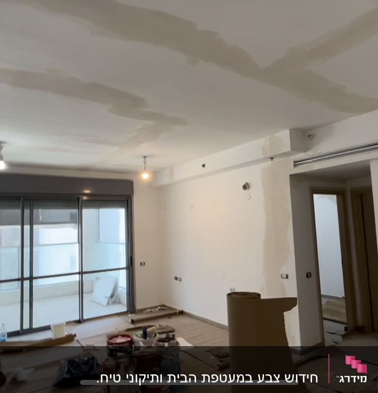 חדר עם קירות לבנים, פחיות צבע וכלי עבודה על הרצפה